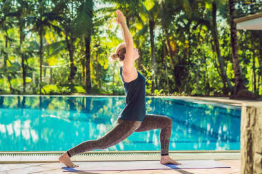 美丽的年轻快乐的女人做瑜伽运动附近的游泳池。健康的生活方式和良好的健康概念