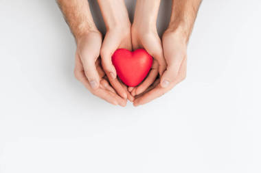 老年人手的頂部和小一抱著紅色的心在白色背景隔離