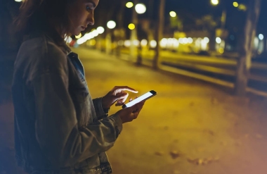 女人指著屏幕上的智能手機(jī)背景照明散燈在夜間大氣城市, 時(shí)髦使用手手機(jī)特寫, 在巴塞羅那的模型閃閃發(fā)亮的街道, 在線 wifi 互聯(lián)網(wǎng)概念