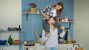 快乐的年轻夫妇在厨房的乐趣在家里。女孩坐在男朋友脖子上