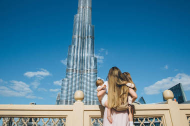 幸福美丽的母亲与她可爱的小女儿的肖像考虑惊人的阿拉伯建筑, 哈里发塔对蓝天, 迪拜, 阿联酋