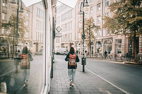 带背包的年轻女子穿着运动和休闲在一个城市的蓝色牛仔裤和蓝色毛衣, 并在夏天的商店橱窗反射
