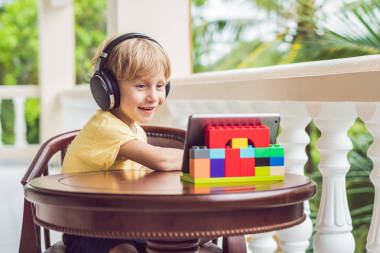 在热带的可爱的男孩与朋友和家人聊天使用平板电脑和无线耳机在阳台上进行视频通话