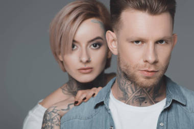 近距離肖像的時(shí)尚年輕情侶與紋身看著相機(jī)孤立在灰色