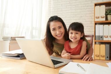快樂的亞洲母親與她的小女兒在桌子上的筆記本電腦