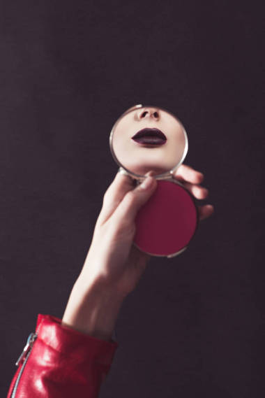 裁剪圖像的迷人的女孩與黑暗的嘴唇看著鏡子隔離在棕色