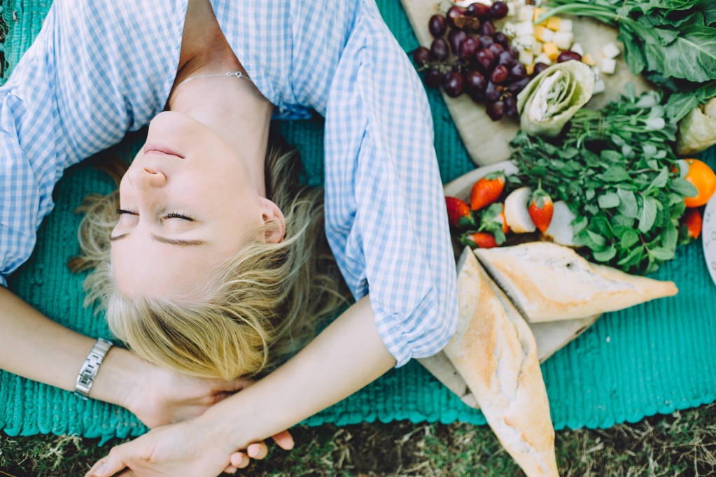 夏日野餐放松的年轻女子躺在垫子上, 健康的食物