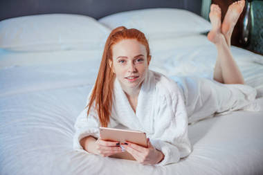 美麗的婦女穿著浴衣和使用數(shù)字片劑, 而在床上休息