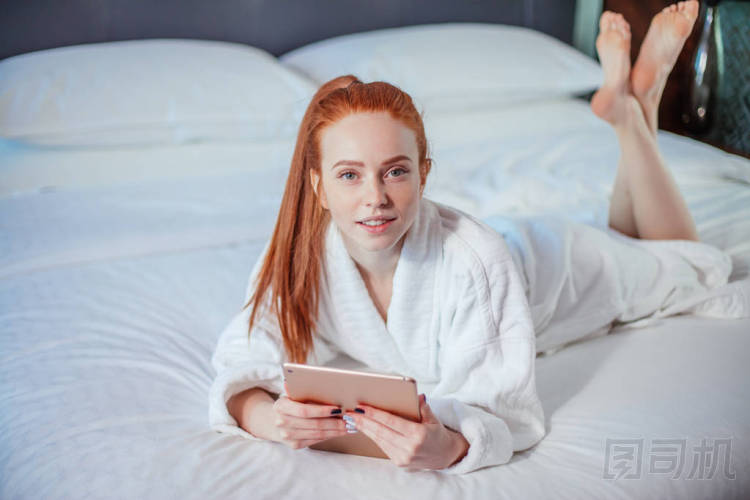 美麗的婦女穿著浴衣和使用數(shù)字片劑, 而在床上休息