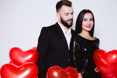 美丽的年轻情侣在爱情的黑色优雅的服装背景下的红色气球的形状一颗心。情人