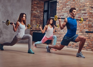 兩個(gè)健身婦女和一個(gè)教練, 伸展蹲與杠鈴在俱樂部?jī)?nèi)部閣