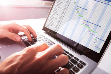 在辦公用筆記本電腦上的甘特圖上工作的商人的手關(guān)閉