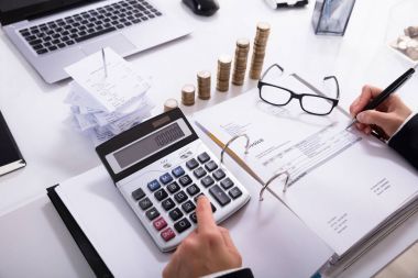 堆積硬幣和筆記本電腦在女實(shí)業(yè)家前面使用計(jì)算器在辦公室計(jì)算發(fā)票