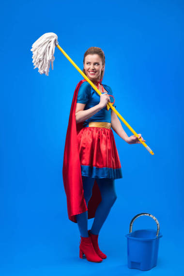微笑的婦女在超級(jí)英雄服裝用拖把和桶清洗隔離在藍(lán)色