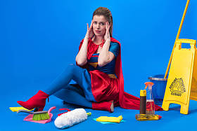 疲惫的女人在超人服装与清洁用品周围隔离蓝色