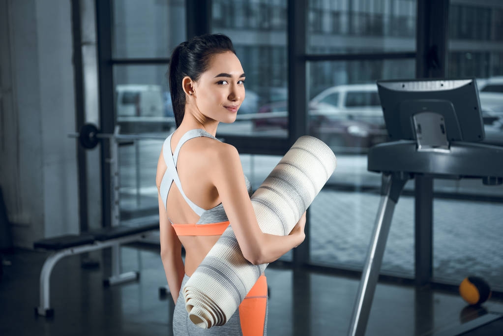 年轻的运动妇女与滚动瑜伽垫在健身房 年轻的运动妇女与滚动瑜伽垫在健身房