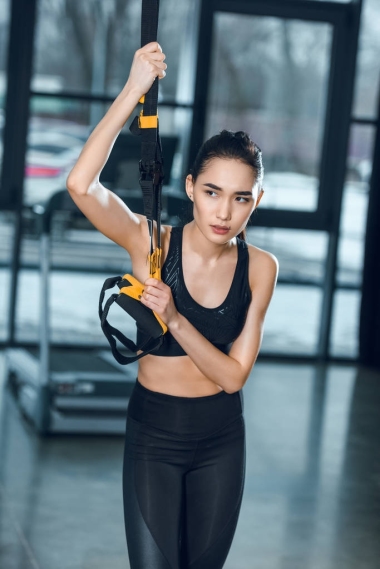 年輕運動的婦女鍛煉放松在健身房, 而靠在懸掛帶