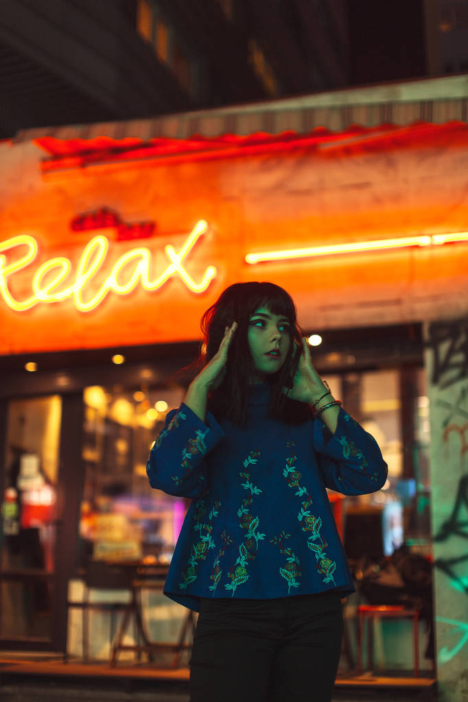 年轻的日本女孩站在霓虹灯附近, 摆出照相机的姿势