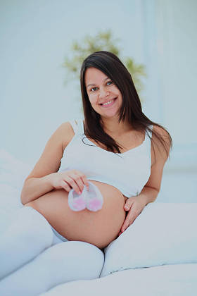 孕妇微笑和拿着未来婴儿袜子