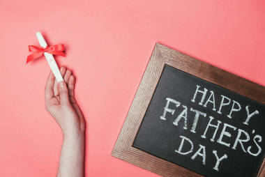 婦女舉行妊娠試驗(yàn)帶絲帶和快樂(lè)父親日的裁剪拍攝在黑板上的字體在粉紅色隔離