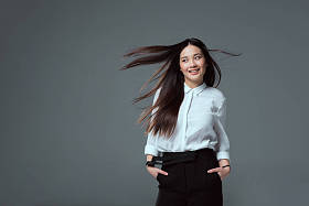 美丽的微笑亚洲女孩站在口袋里的手, 看着远离孤立的灰色