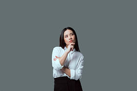 若有所思的年轻女子站在下巴上的手, 看着远离孤立的灰色