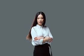 美丽的亚洲女孩站在交叉的武器和看着相机孤立灰色