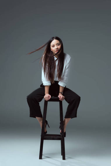 美麗的年輕亞洲婦女坐在椅子上, 看著在灰色相機
