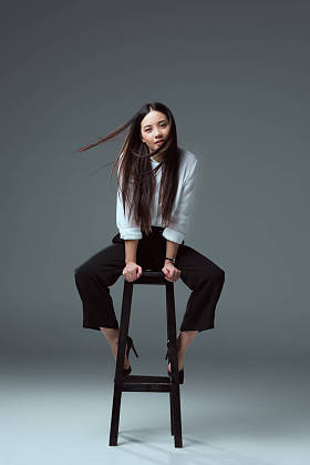 美丽的年轻亚洲妇女坐在椅子上, 看着在灰色相机
