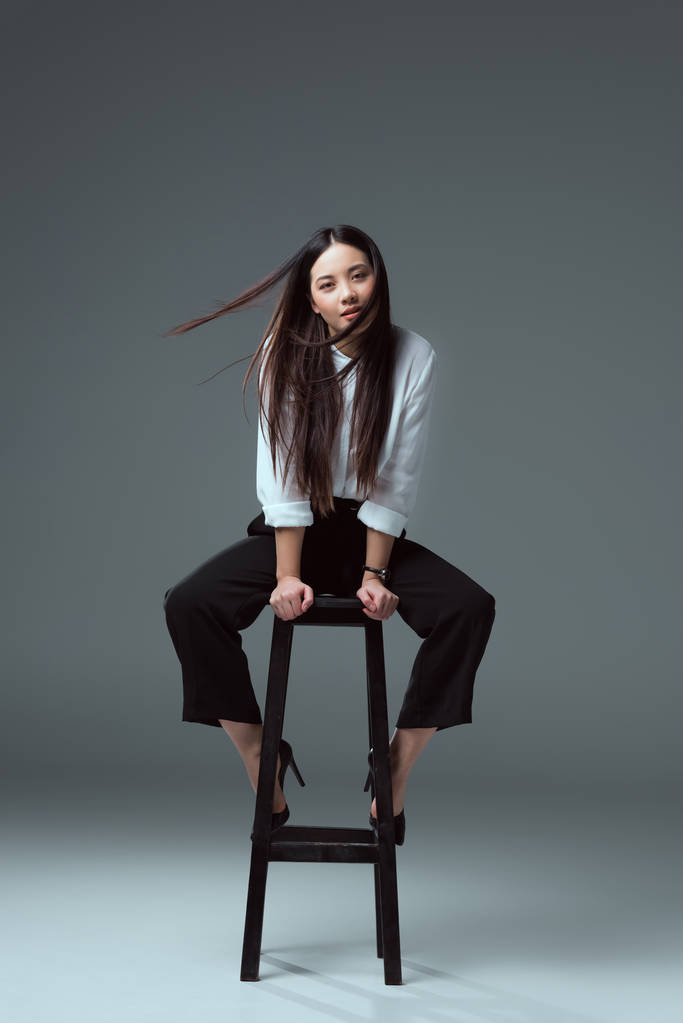 美丽的年轻亚洲妇女坐在椅子上, 看着在灰色相机