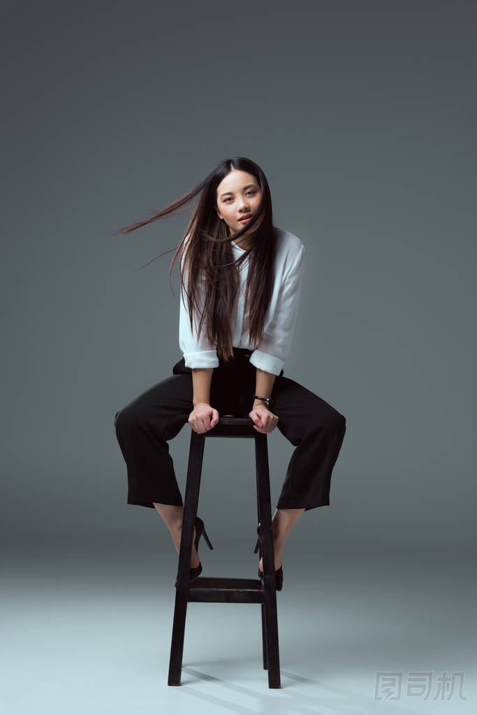 美麗的年輕亞洲婦女坐在椅子上, 看著在灰色相機(jī)