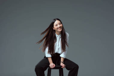 迷人的亞洲女孩坐在椅子上, 微笑著在鏡頭上的灰色隔離