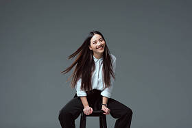迷人的亚洲女孩坐在椅子上, 微笑着在镜头上的灰色隔离