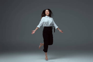 愉快的赤足女孩跳躍和微笑在照相機在灰色