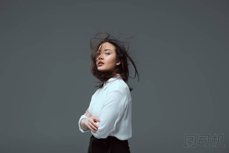 有吸引力的年輕亞洲婦女的肖像站在交叉的武器和看著相機孤立灰色
