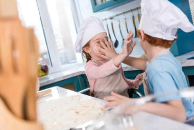 有選擇的焦點可愛的小孩子在廚師帽子有樂趣與面粉在廚房