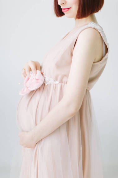 幸福的孕婦站立抱著粉紅色的鞋子為嬰孩, 莊稼的外形視圖