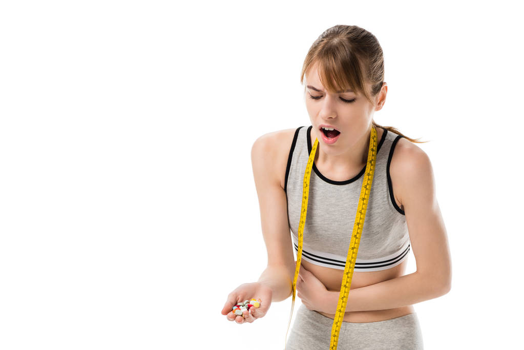 年轻的女人与胃痛举行堆药片隔离在白色