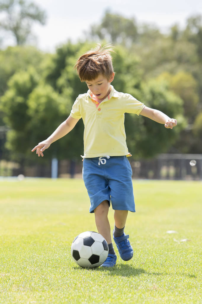 小孩子7或8岁享受快乐踢足球足球在草市公园田野奔跑和踢球兴奋的童年运动激情