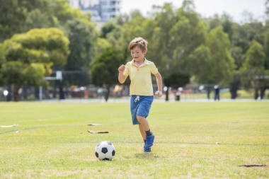 小孩子7或8歲享受快樂踢足球足球在草市公園田野奔跑和踢球興奮的童年運動激情