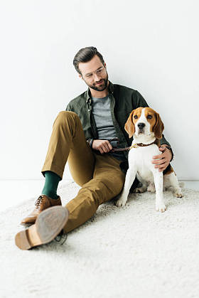 英俊的男子拥抱可爱的猎犬在地毯上
