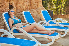 热带度假胜地的比基尼女子日光浴。美丽的女人躺在太阳躺椅