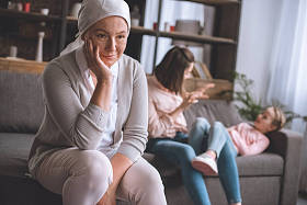 微笑生病成熟的女人在头巾看着, 而家庭成员有乐趣背后