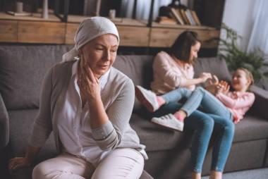 生病成熟的女人在頭巾看著, 而家庭成員有樂(lè)趣背后