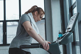 肥胖女孩休息在跑步机在健身房