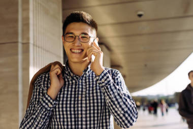 年輕的亞洲男人微笑著在城市里漫步, 在電話和微笑中交談