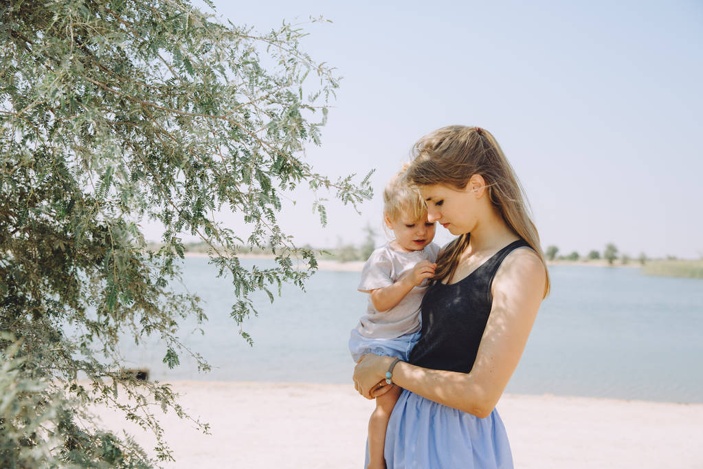 美丽的年轻母亲与她可爱的小女儿附近的树室外阳光明媚的一天 美丽的年轻母亲与她可爱的小女儿附近的树室外阳光明媚的一天