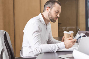 嚴(yán)肅的建筑師與紙杯咖啡使用智能手機(jī)在辦公室