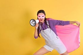 在黄色背景扩音器的超级英雄服装的年轻女子