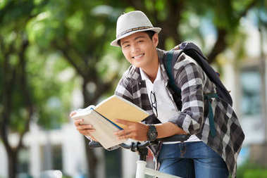 微笑著的大學(xué)生倚著車把看書照片